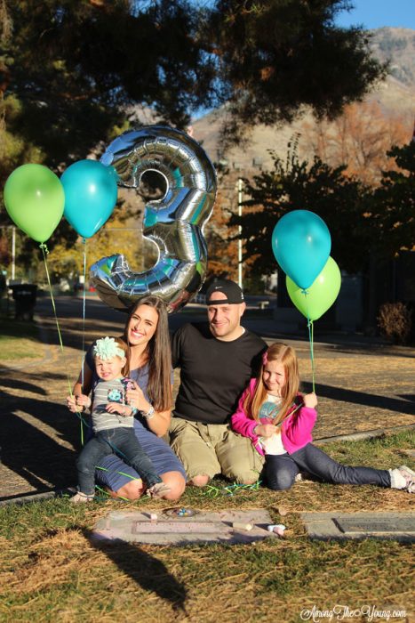 sibling loss featured by top Utah lifestyle blog, Among the Young: image of third birthday | Sibling Loss: 7 Essential Tips to Help your Child Grieve by popular Utah lifestyle blog, Among the Young: image of a family kneeling by a headstone and holding birthday balloons.
