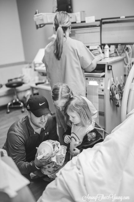 Baby girl birth story by top Utah lifestyle blog, Among the Young: image of girls meeting the baby | Birth Story by popular Utah motherhood blog, Among the Young: black and white image of two young girls looking at their newborn sister as their dad holds her. 