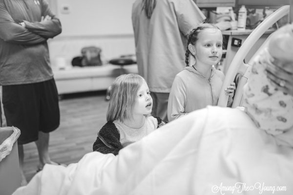 Baby girl birth story by top Utah lifestyle blog, Among the Young: image of girls seeing the baby | Birth Story by popular Utah motherhood blog, Among the Young: black and white image of two young girls looking at their newborn sister. 