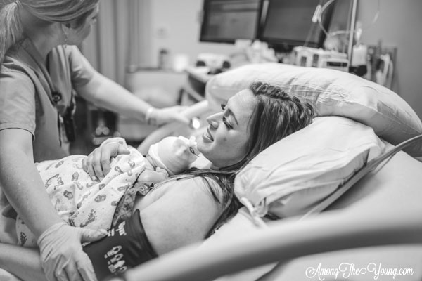 Baby girl birth story by top Utah lifestyle blog, Among the Young: image of mom getting checked after baby | Birth Story by popular Utah motherhood blog, Among the Young: black and white image of a woman laying in a hospital bed while holding her newborn baby on her chest. 