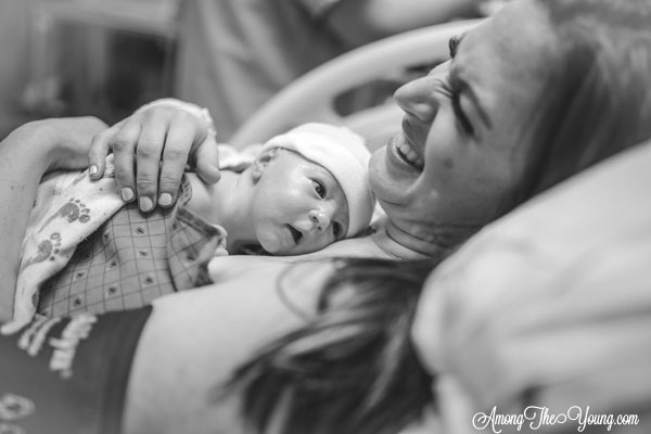 Baby girl birth story by top Utah lifestyle blog, Among the Young: image of mom laughing and holding the baby | Birth Story by popular Utah motherhood blog, Among the Young: black and white image of a woman laying in a hospital bed while holding her new born baby on her chest. 